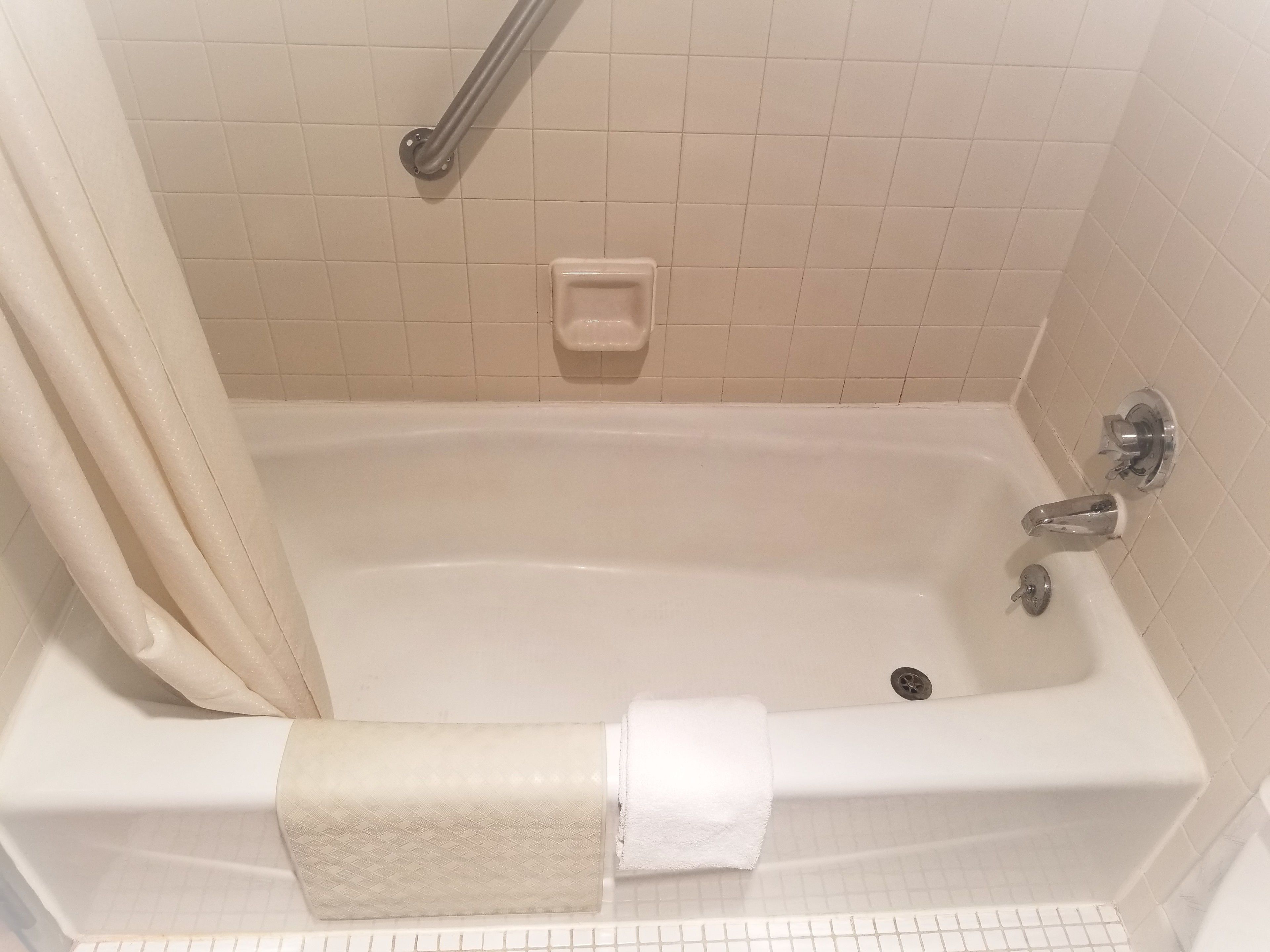 Eine Standardbadewanne mit einer Haltestange, einer Handbrause und einem Handtuchhalter.
