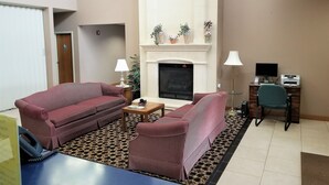 A living room with a fireplace, two striped sofas, a coffee table, and a desk with a computer. - Abby Inn (Abbotsford)