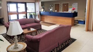 A reception area with a counter, two sofas, a lamp, and a patterned rug. - Abby Inn (Abbotsford)