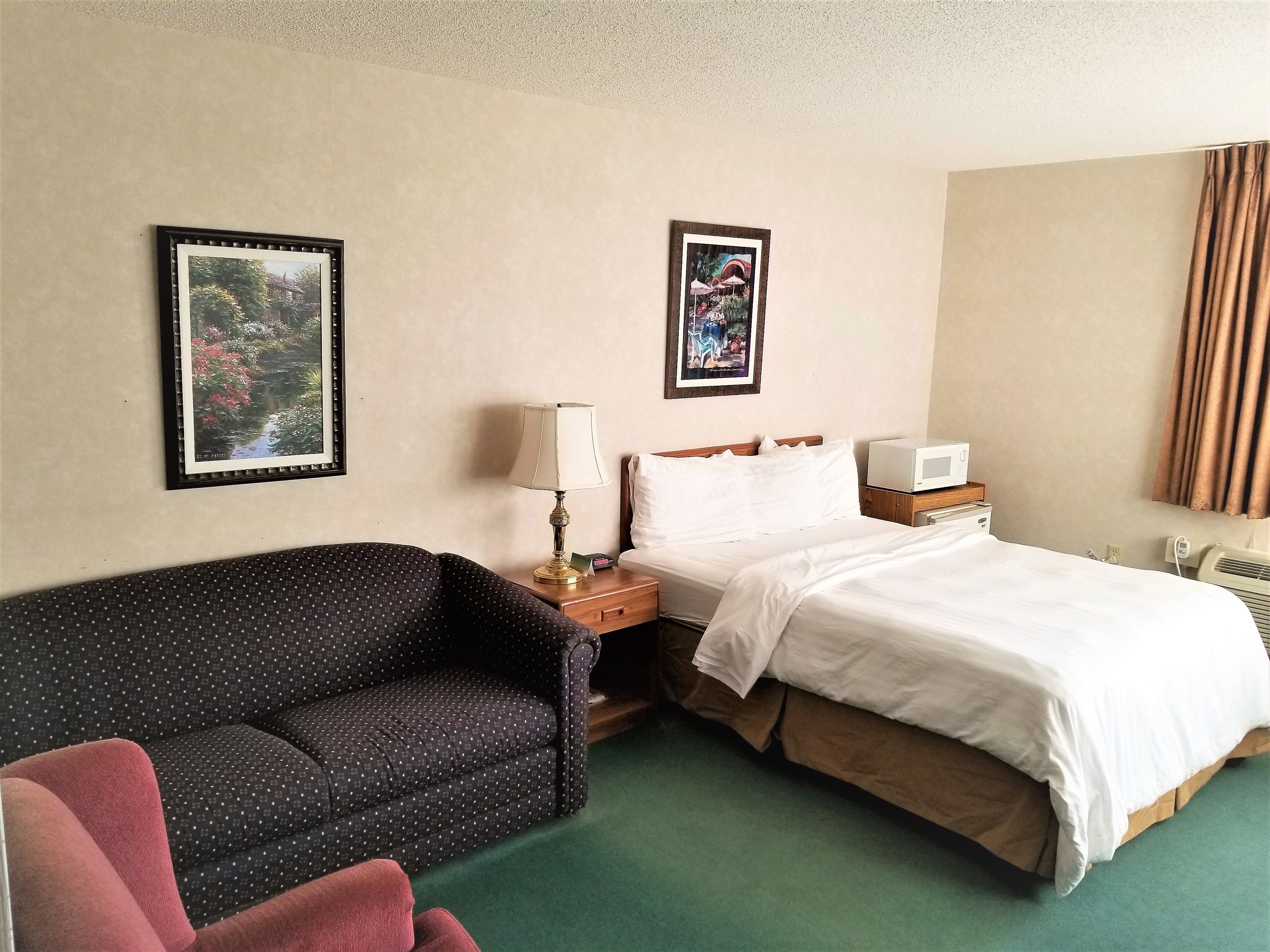 A hotel room with a bed, a nightstand, a lamp, a framed picture on the wall, and a couch.