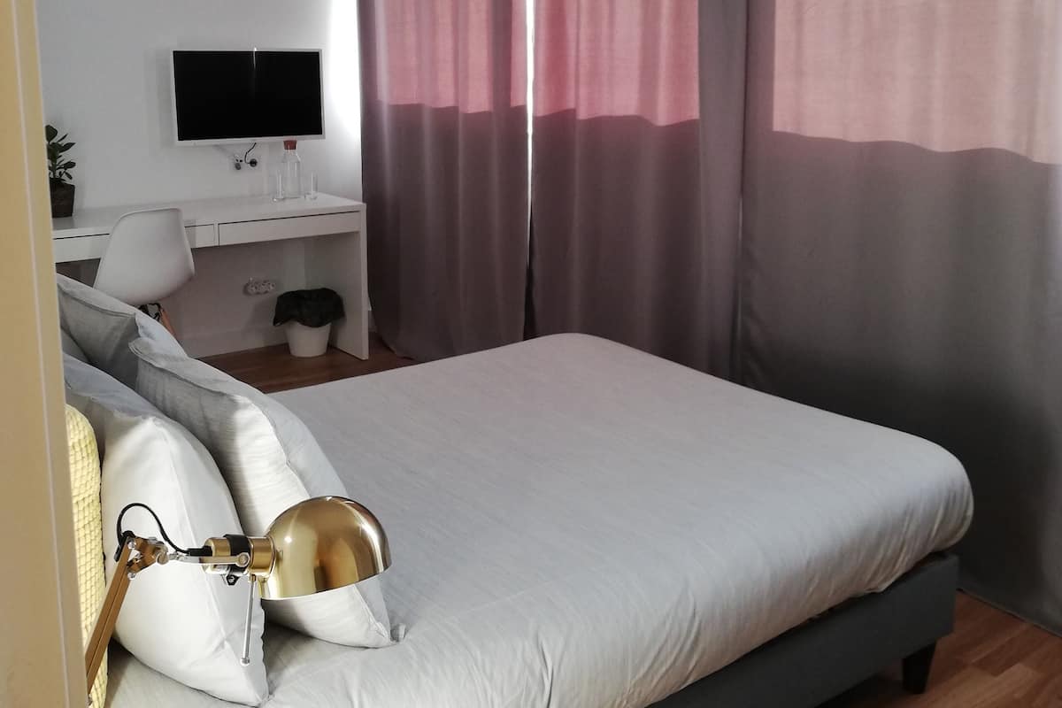 A modern bedroom with a large bed, a bedside table with a lamp, a flat-screen TV, and a desk with a chair.
