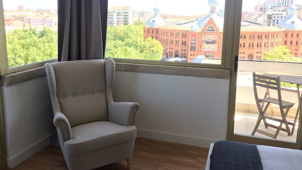 A room with a large window, a chair, and a small table. - Republica83-Campo Pequeno Home (Lisbon)