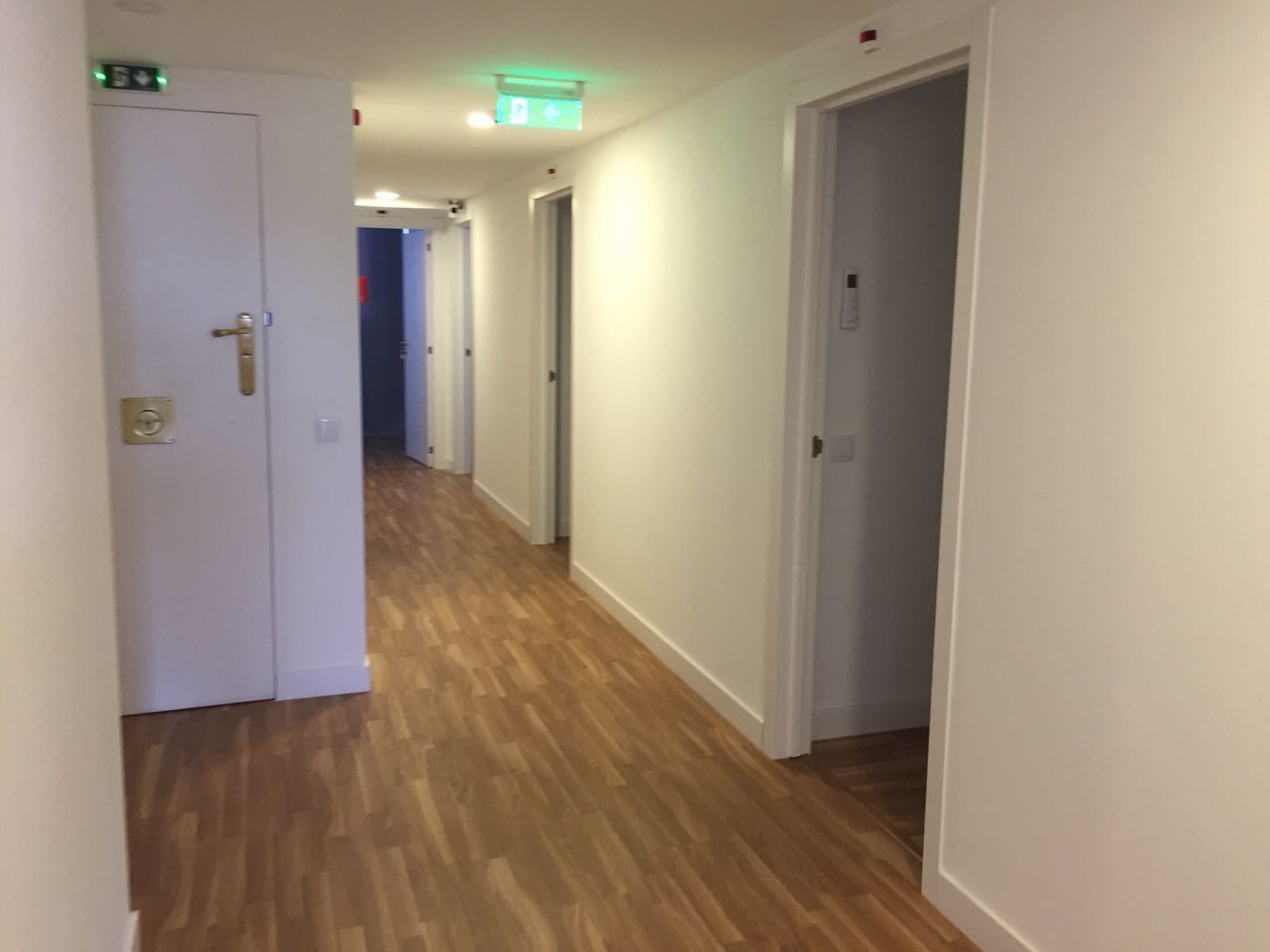 A corridor with wooden flooring and white walls, leading to multiple doors.