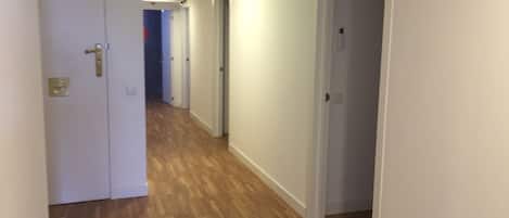 A corridor with wooden flooring and white walls, leading to multiple doors.
