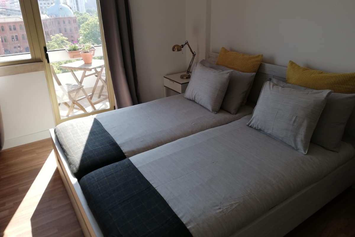 A bedroom with a large bed, a nightstand, a lamp, and a view of the city through a window.