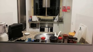 A compact kitchen with a microwave, stove, and sink. There is a window above the sink and a refrigerator to the right. - Republica83-Campo Pequeno Home (Lisbon)
