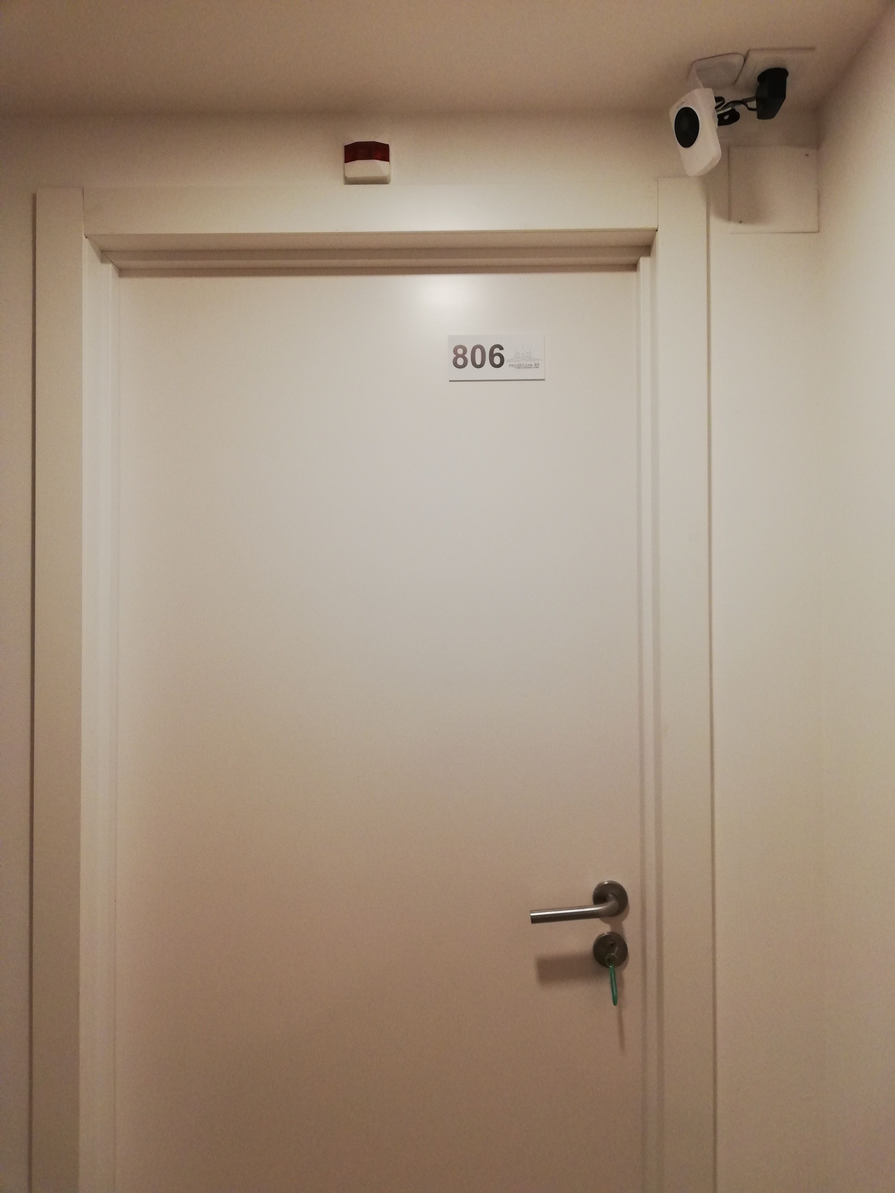 Porta fechada com placa numerada 806, maçaneta e pequena luminária acima.