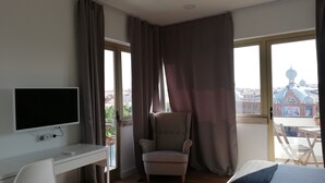 A hotel room with a desk, chair, bed, and large windows offering a view of a cityscape. - Republica83-Campo Pequeno Home (Lisbon)