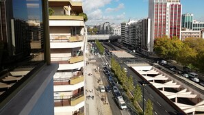 A high-rise building with multiple balconies, a busy street with cars and pedestrians, and other modern buildings in the background. - Republica83-Campo Pequeno Home (Lisbon)