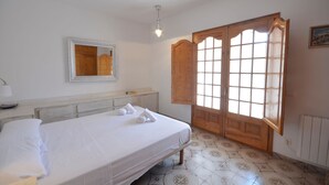 A bedroom with a bed, a mirror, a wooden wardrobe, and a window with curtains. - Holiday rental townhouse with swimming pool in Begur, Centre (Begur)