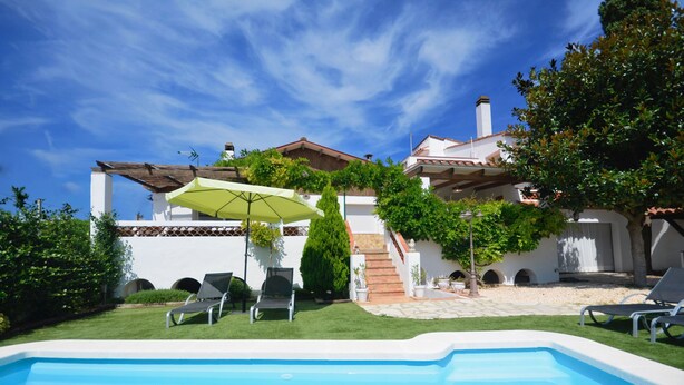A pool area with lounge chairs and a green umbrella, surrounded by a white building with a tiled roof and a staircase leading to a second level. - Holiday rental townhouse with swimming pool in Begur, Centre (Begur)