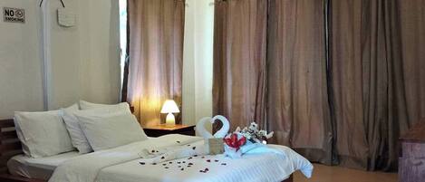 A bedroom with a bed, curtains, a ceiling fan, an air conditioning unit, and a bedside table with a lamp.