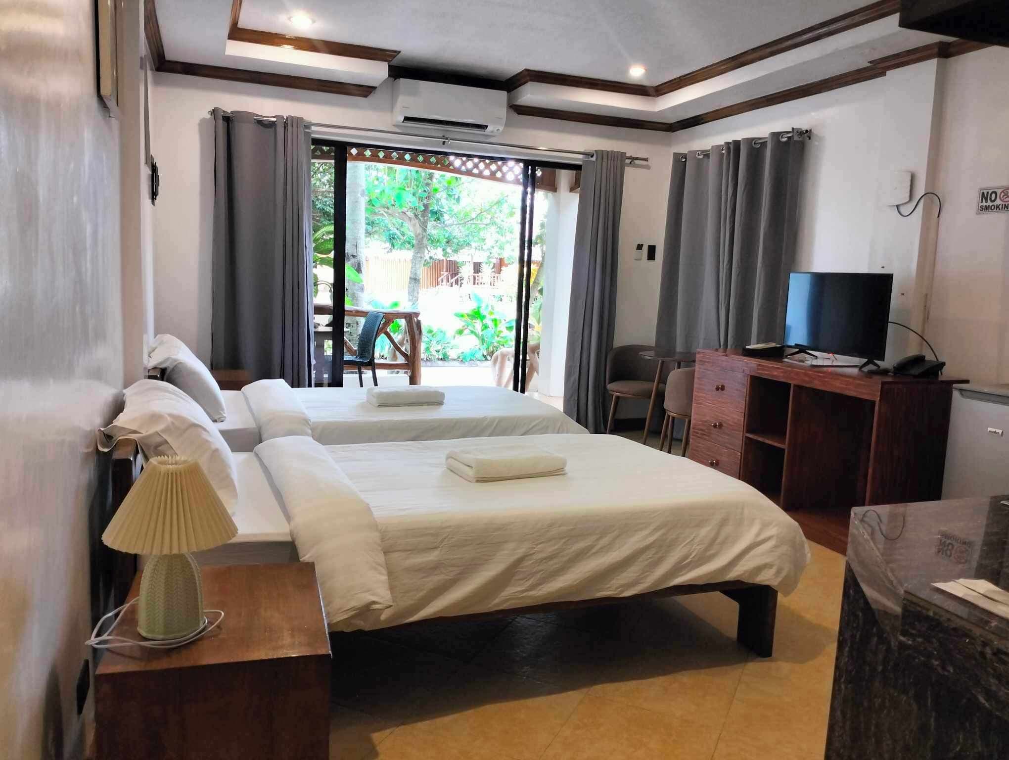 A hotel room with a bed, a desk with a TV, and a view of the outdoors.