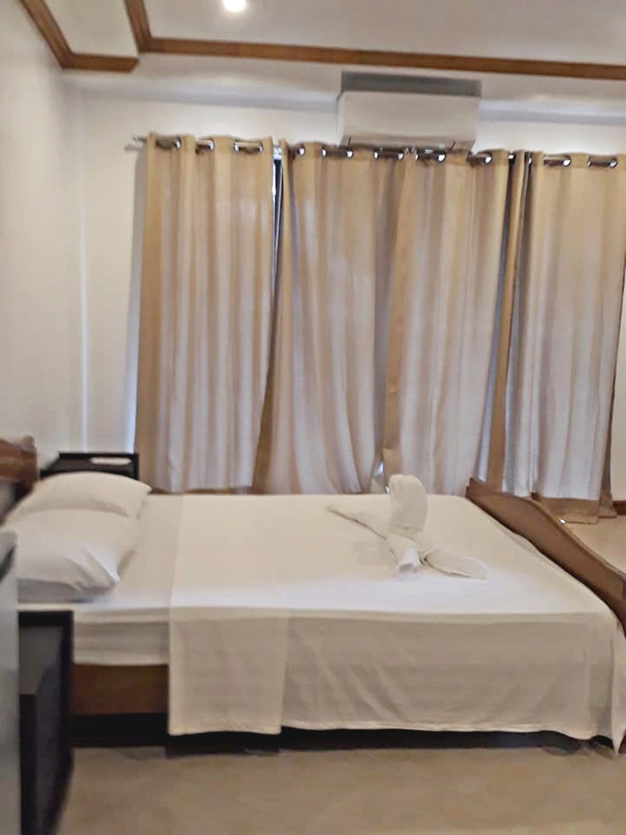 Een hotelkamer met een bed, nachtkastje, spiegel en beige gordijnen.