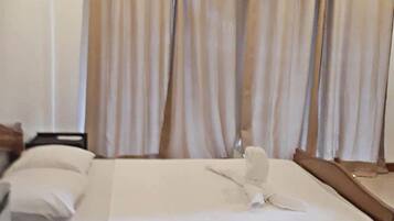 Een hotelkamer met een bed, nachtkastje, spiegel en beige gordijnen.