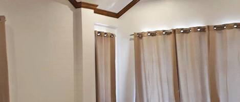 A bedroom with a wooden bed, white bedding, a ceiling fan, and curtains.