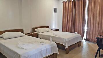 A hotel room with two single beds, a small table, and a chair.