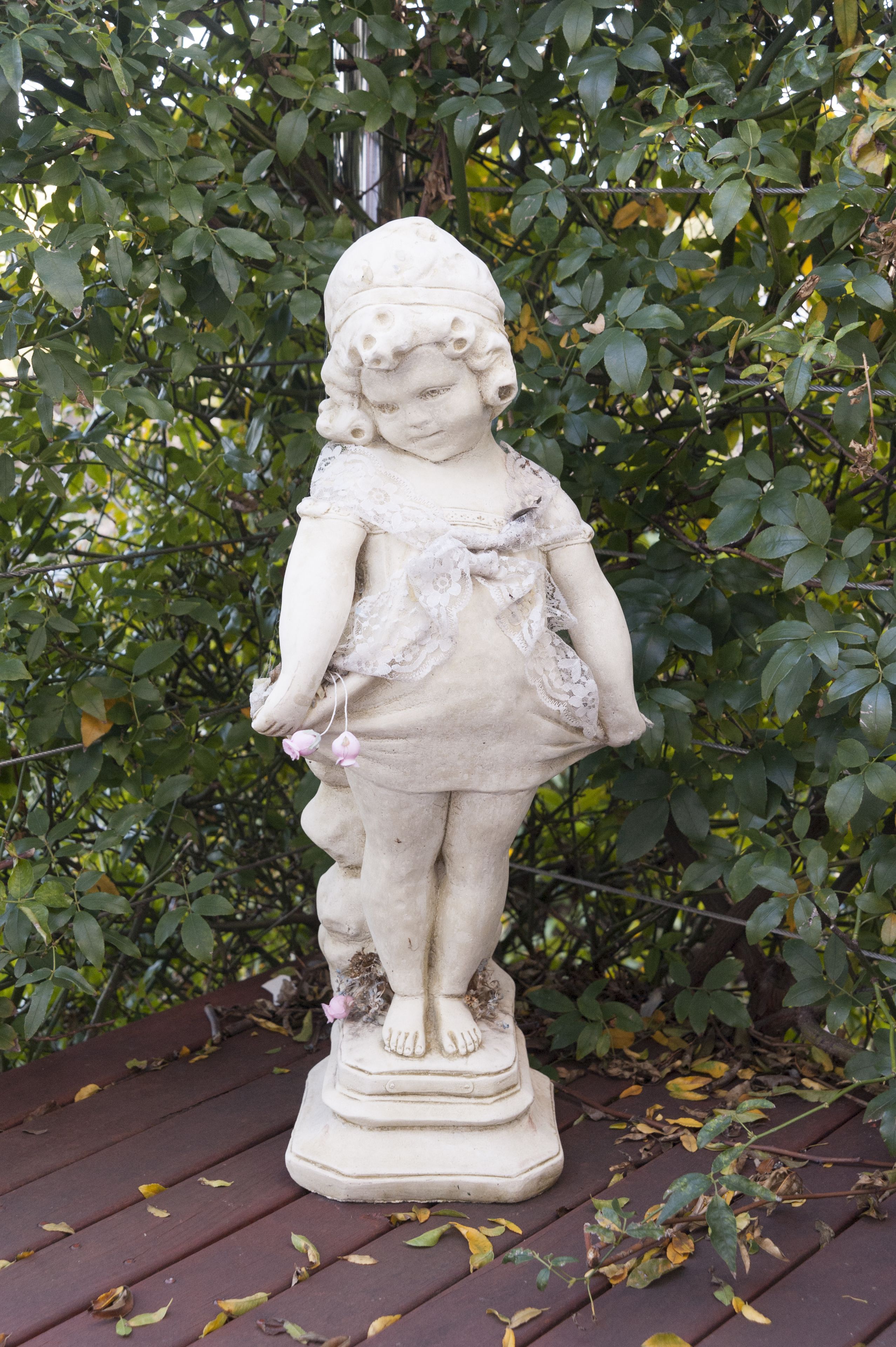Una estatua de un niño sobre una plataforma de madera, rodeada de follaje.