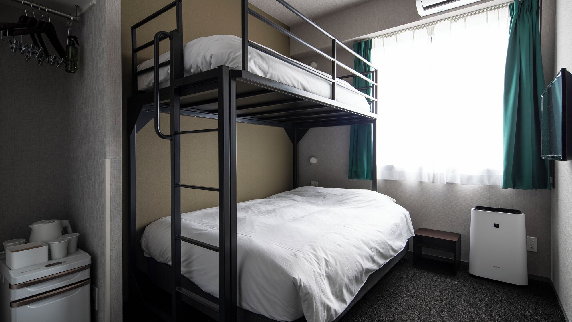 A bunk bed room with a desk, a kettle, and a small heater.
