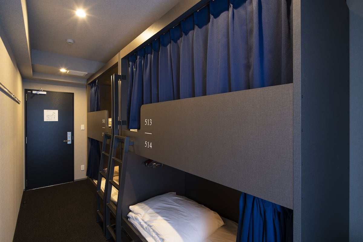 Een hotelkamer met stapelbedden, genummerd 513 en 514, een deur met een bordje en een plafondlamp.