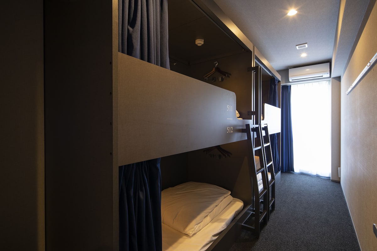 Een slaapkamer met een stapelbed, raam, gordijnen en een kledingroede.