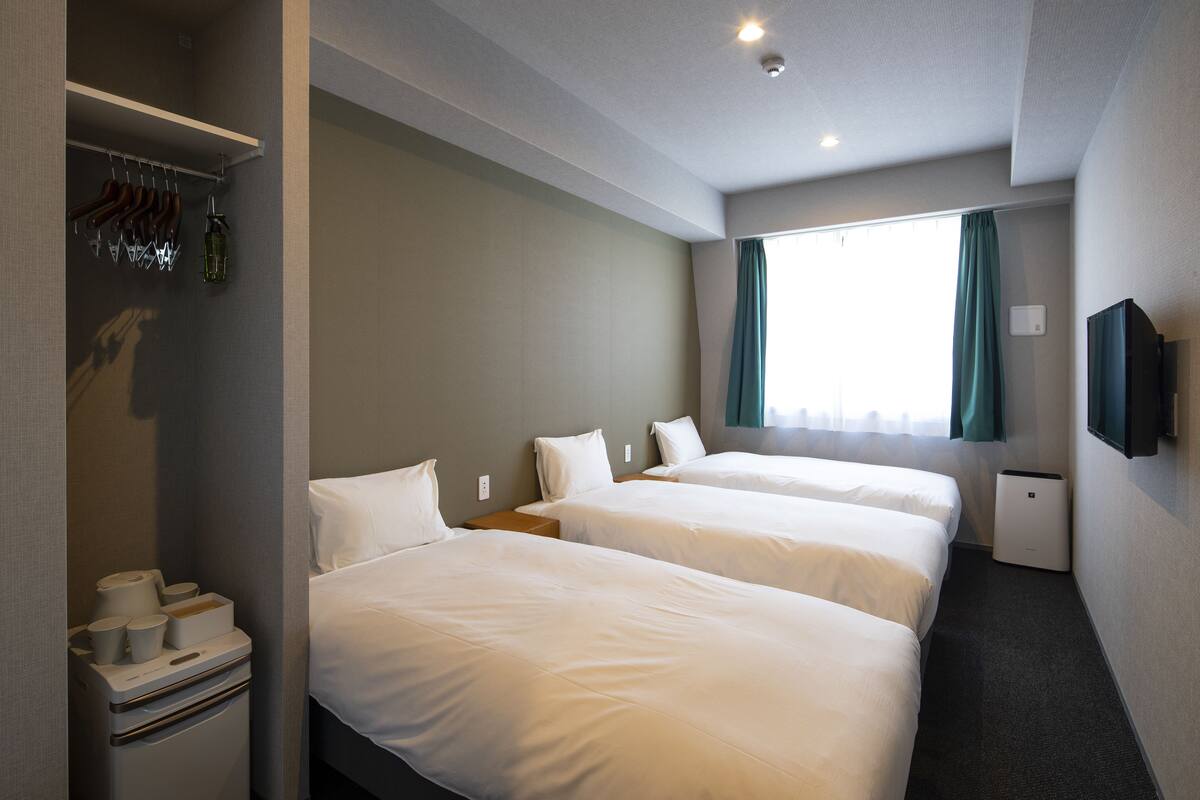 Een hotelkamer met twee bedden, een kledingkast, een televisie en een raam met gordijnen.