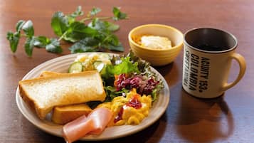 A plate of food with toast, ham, scrambled eggs, and a salad, accompanied by a mug and a bowl of butter.