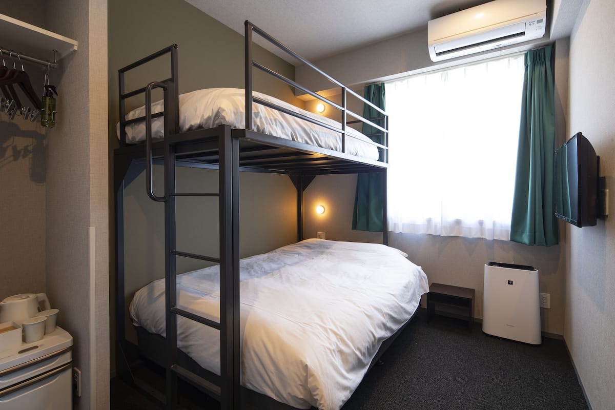 Een slaapkamer met een stapelbed, een bureau, een stoel, een airconditioner en een raam met gordijnen.