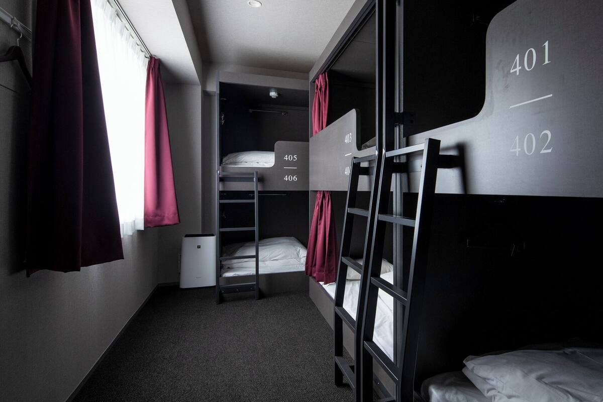 Een slaapkamer met stapelbedden, genummerde bedden, een kleine kast en een raam met gordijnen.