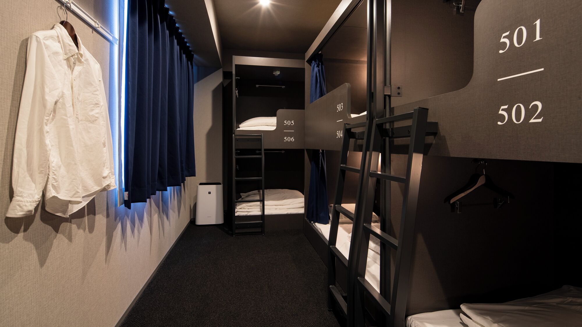 A compact hotel room with bunk beds, a small desk, and a hanging coat rack.
