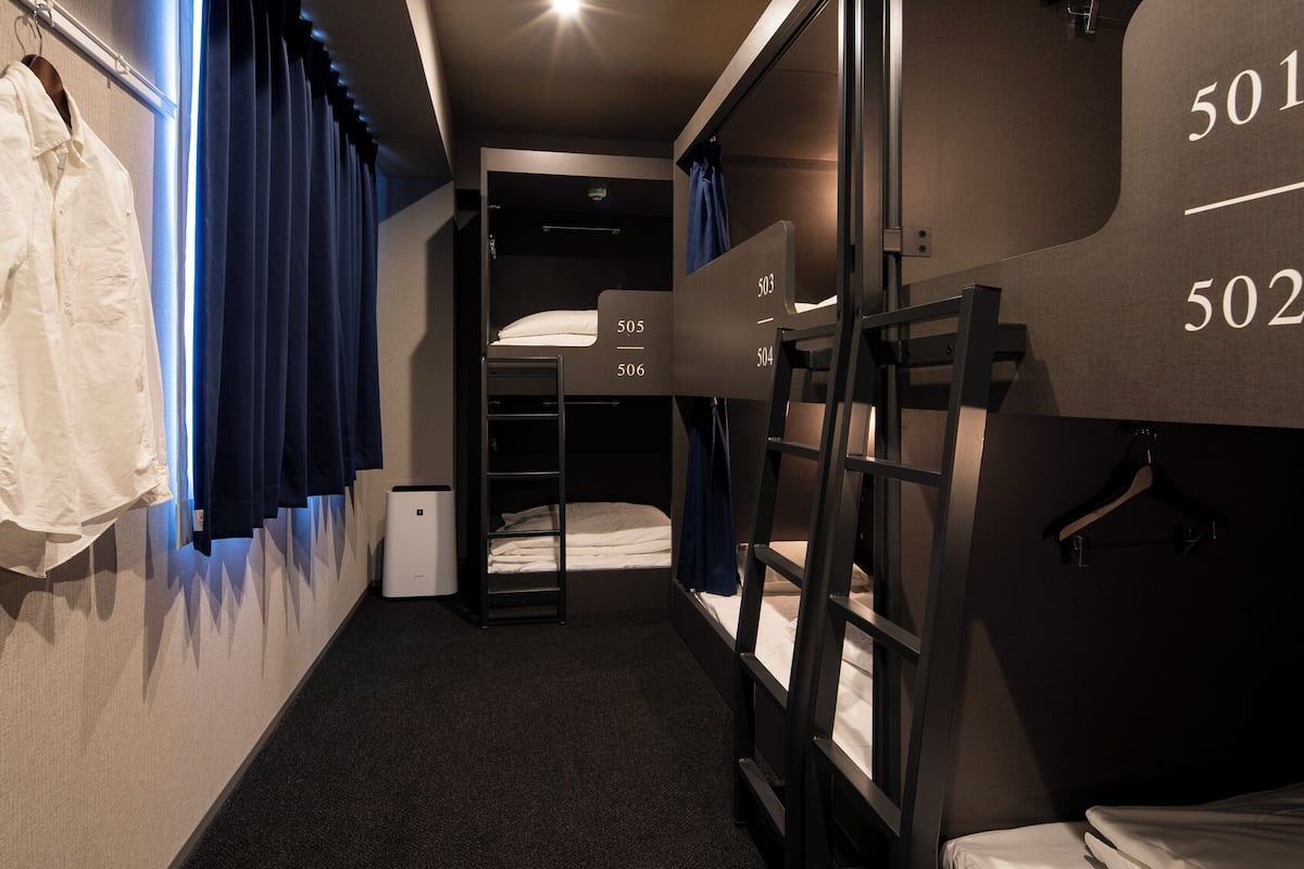 Ett kompakt hotellrum med våningssängar, ett litet skrivbord och en klädstång.