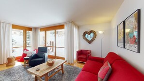 Ein Wohnzimmer mit einem roten Sofa, einem schwarzen Sessel, einem Holztisch und einer herzförmigen Wanddekoration.