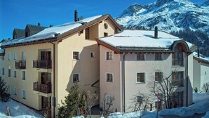 Ein zweistöckiges Gebäude mit Balkonen, einem mit Schnee bedeckten Dach und Bergelandschaft im Hintergrund.