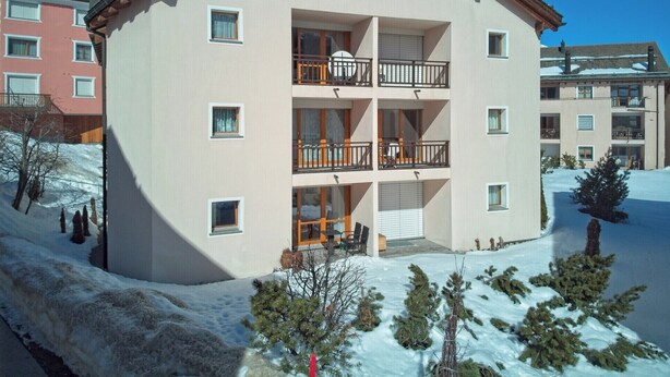 Ein mehrstöckiges Hotel mit Balkonen, eine verschneite Landschaft und Berge im Hintergrund.