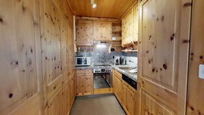 A narrow kitchen with wooden cabinets, a microwave, a stove, and a sink. - Quiet 2-room apartment, ca. (Sils/Segl Maria)