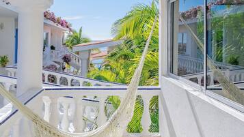 A balcony with a white railing, a hammock, and a view of a building with balconies and plants.