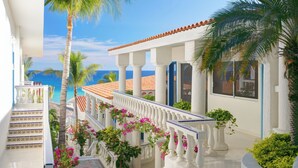 A white building with a balcony, palm trees, and a view of the ocean.