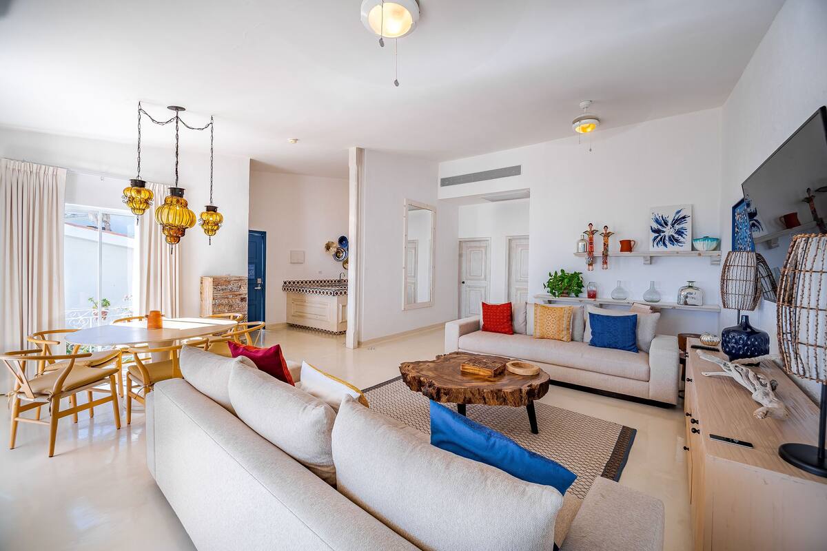 Een ruime woonkamer met een grote bank, een houten salontafel en een eethoek met een ronde tafel en stoelen.