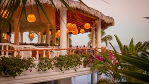 A resort with a thatched-roof pavilion, outdoor seating, and a poolside view.