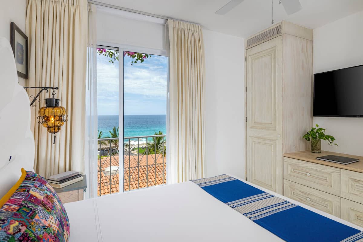 Een slaapkamer met een bed, een televisie, een nachtkastje, een raam met uitzicht op zee en een balkon.
