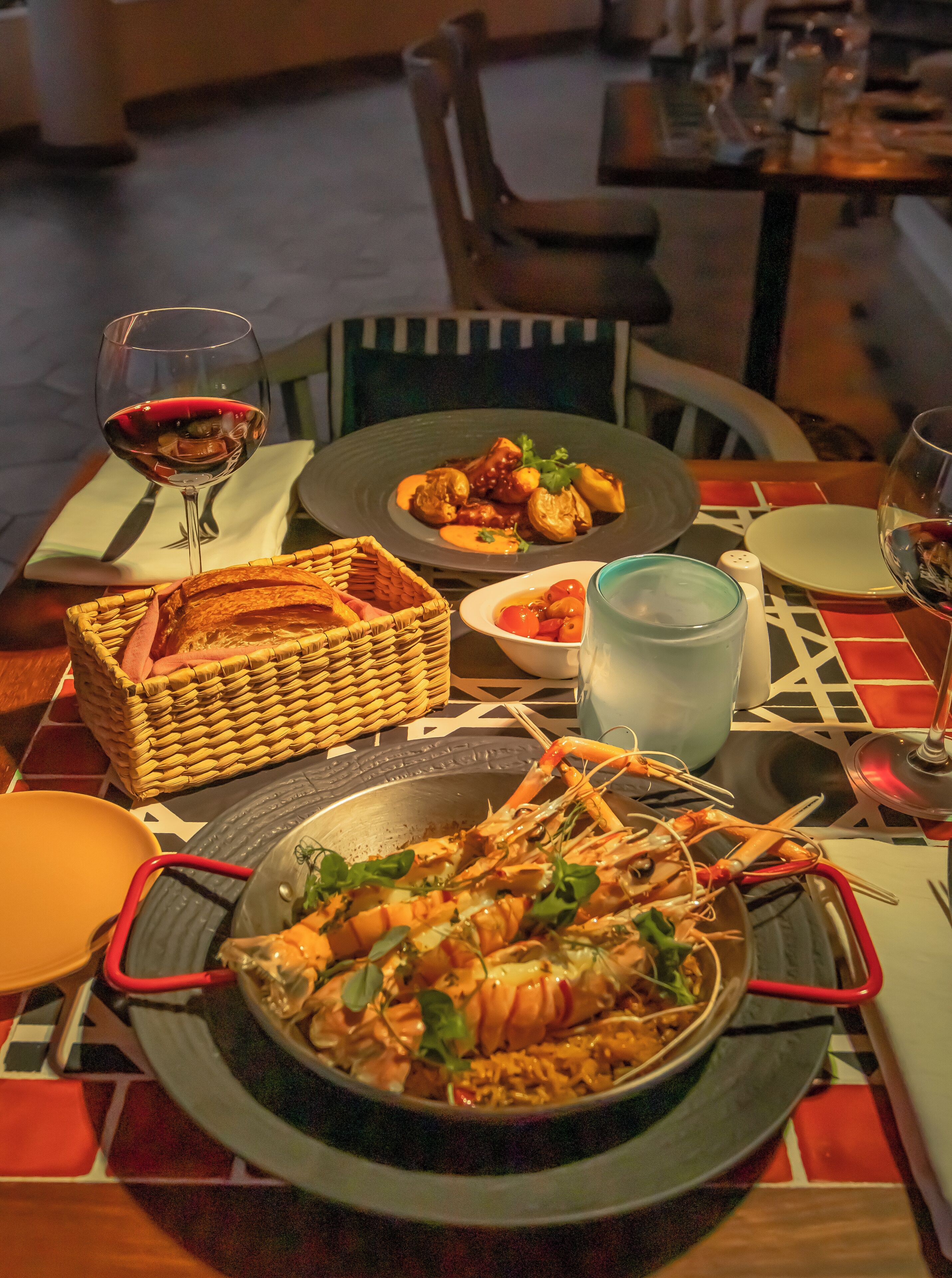 A dining table with plates of food, a basket of bread, and glasses of wine.