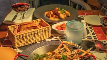 A dining table with plates of food, a basket of bread, and glasses of wine.