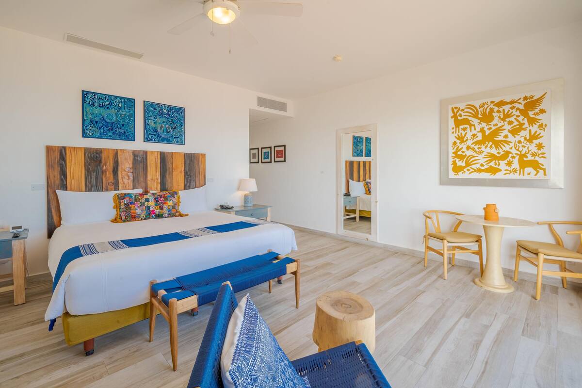 Een moderne hotelkamer met een groot bed, een houten hoofdbord, een kleine tafel met stoelen en kunstwerken aan de muur.