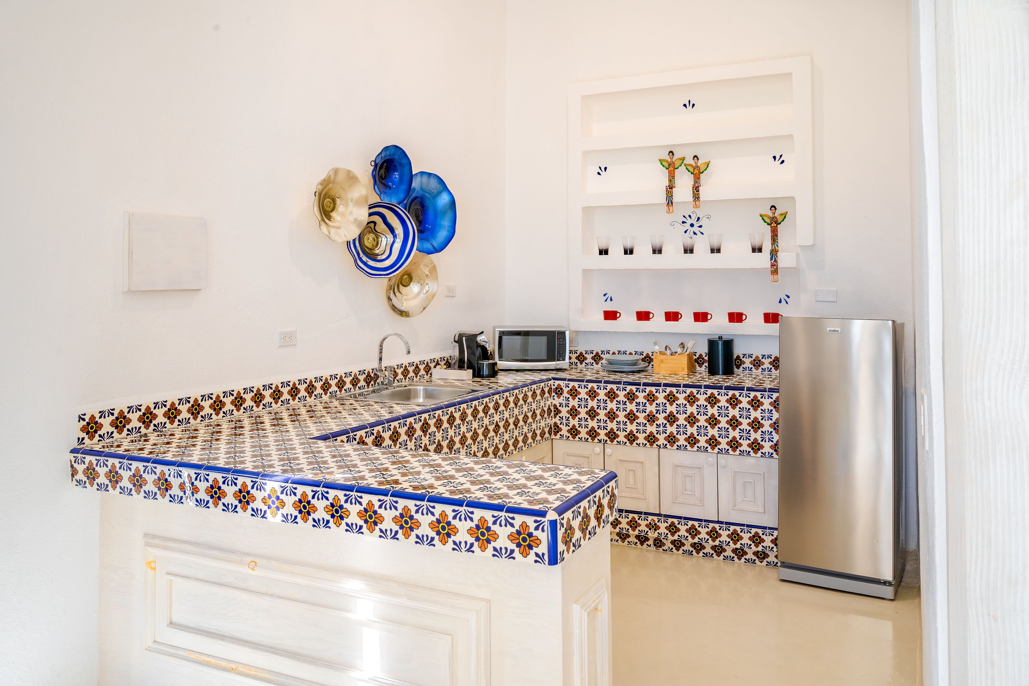 Een keuken met een centraal eiland, witte kasten, een roestvrijstalen koelkast en decoratieve muurkunst.