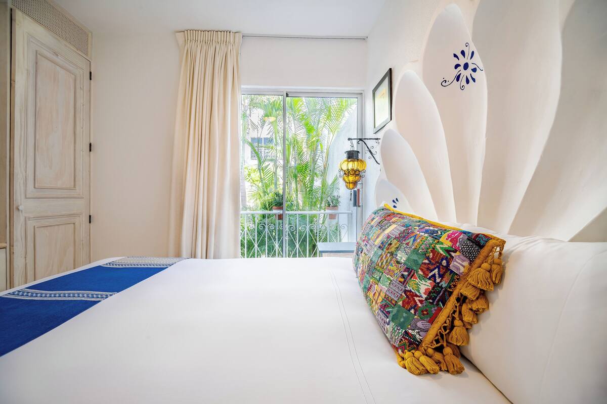 Een slaapkamer met een groot bed, een balkon met uitzicht op groen en een decoratieve wandlamp.