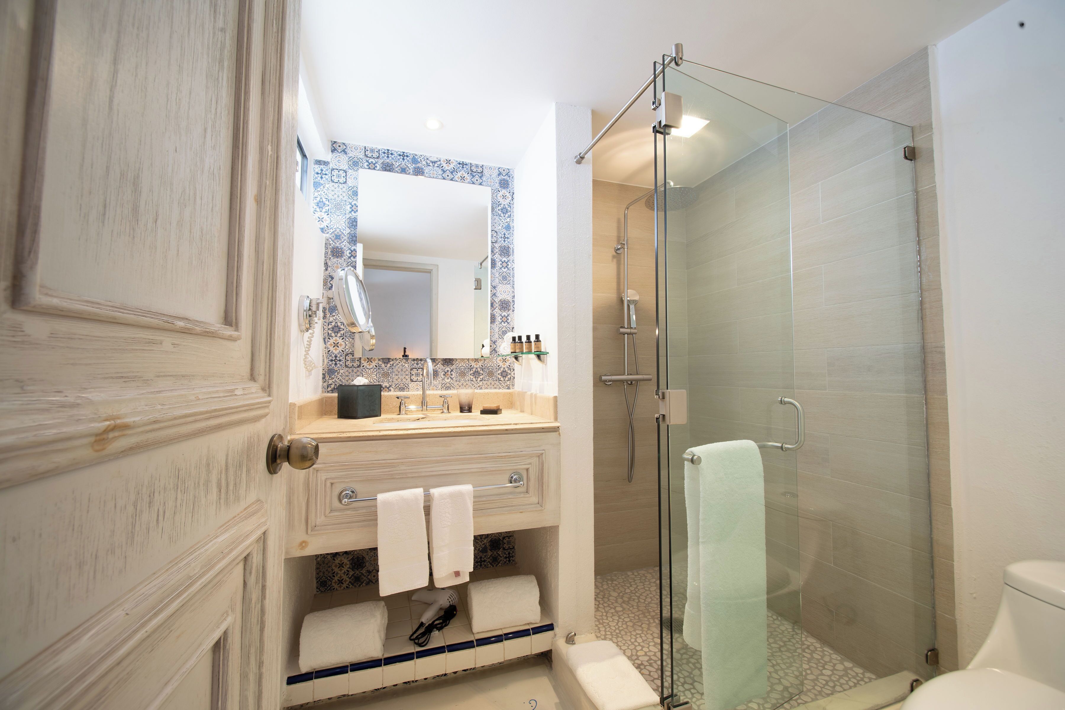 Un baño con puerta de madera, un lavamanos blanco con espejo, cabina de ducha de vidrio y un inodoro.