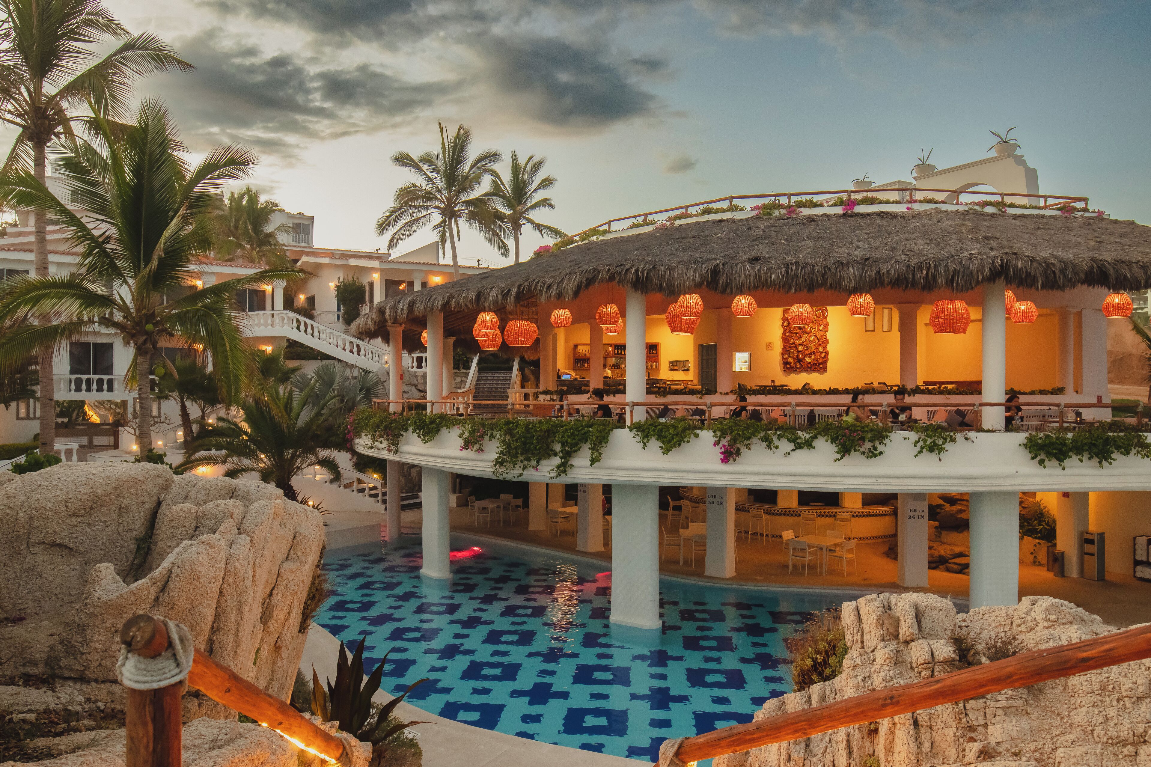 Ein Resort mit Pool, Palmen und einem Restaurant mit einem Reetdach.