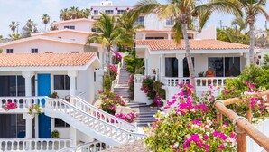 Un bâtiment blanc avec un toit recouvert de tuiles rouges, une porte bleue et un escalier blanc orné de fleurs roses.