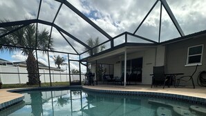 Une piscine à l’eau d’un bleu cristallin, entourée d’un patio abrité avec des chaises et un barbecue.