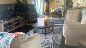 Un salon avec un téléviseur, un canapé, un fauteuil et un panneau d’accueil.